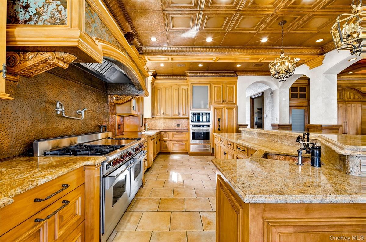 Kitchen featuring an ornate ceiling, stainless steel appliances, light stone counters, decorative backsplash, and arched walkways