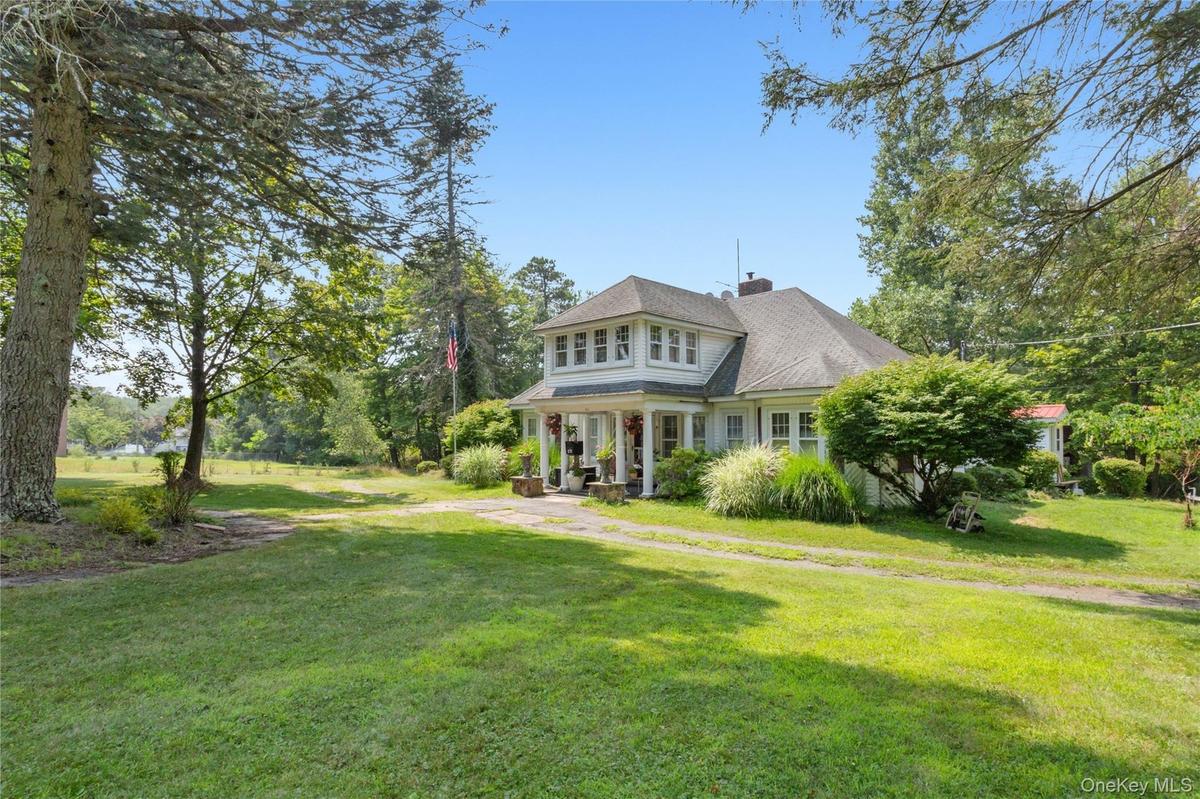 Shingle-style home with a chimney, a front lawn, roof with shingles, and a porch