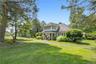 Shingle-style home with a chimney, a front lawn, roof with shingles, and a porch