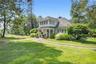 Shingle-style home with a chimney, a front yard, roof with shingles, and covered porch