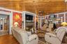 Living room featuring wood ceiling, wood finished floors, ornamental molding, a stone fireplace, and wallpapered walls