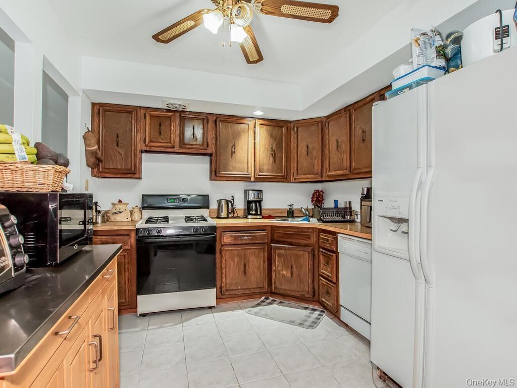 Apt 2 - Kitchen featuring white appliances, ceiling fan, light tile patterned floors, and brown cabinetry