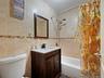 Bathroom featuring a white toilet, a dark wood vanity with a white countertop and rectangular sink, and beige tiled walls with a decorative mosaic acc