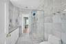 Dual entry Hall Bathroom featuring tiled marble walls and flooring, dual sinks, and  stall shower