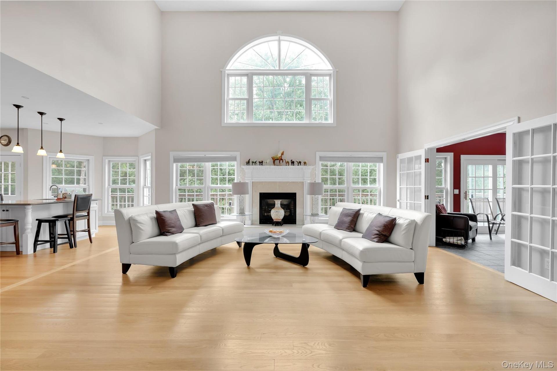 Large family room featuring light oak wood floors, healthy amount of natural light, a towering ceiling, and a glass covered gas fireplace