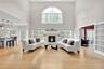 Large family room featuring light oak wood floors, healthy amount of natural light, a towering ceiling, and a glass covered gas fireplace