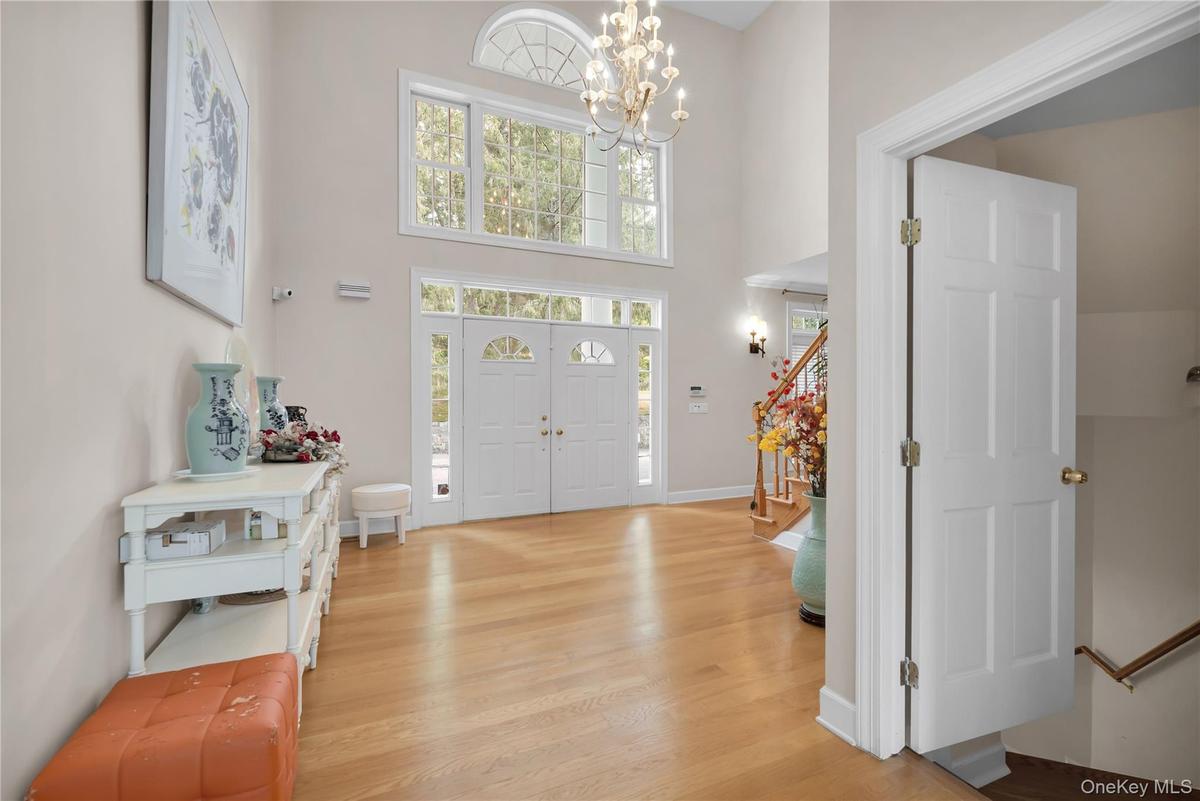 Foyer with a high ceiling, plenty of natural light, light oak wood finished floors, a chandelier, and stairway