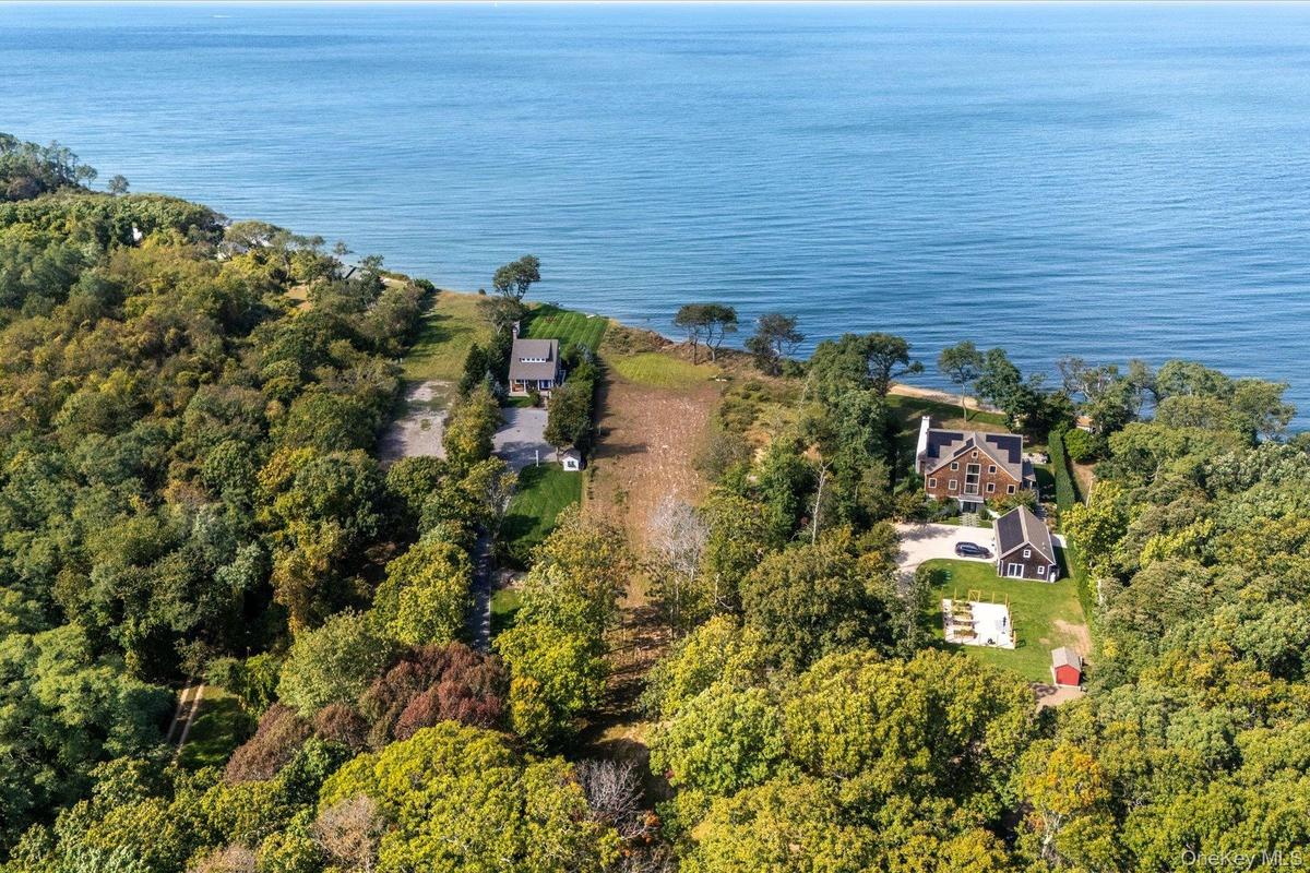 Aerial view highlighting the property's prime position near the waterfront, surrounded by mature trees and neighboring residencees, with the shoreline