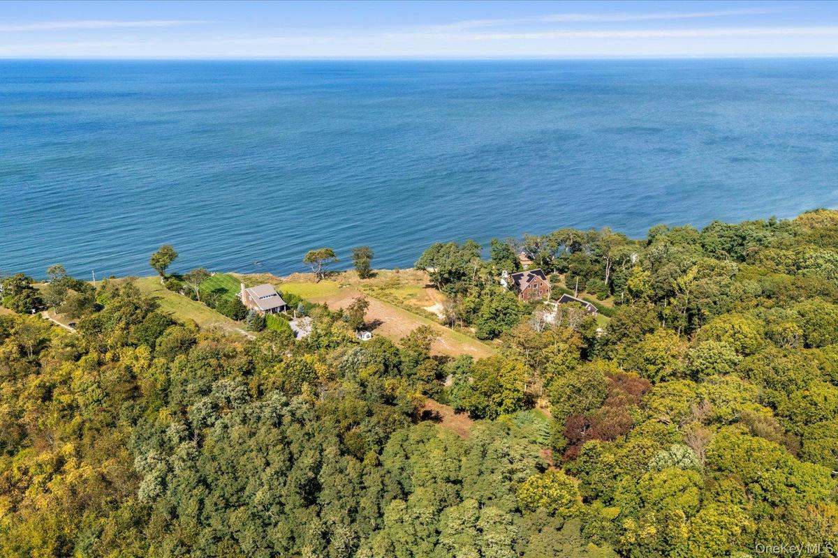 High aerial view showcasing the property's exceptional proximity to the waterfront, surrounded by mature trees and neighboring properties, with expans