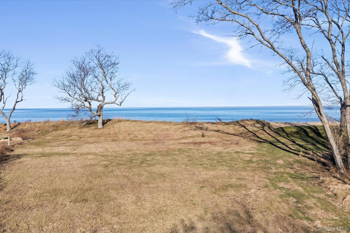 Expansive open lawn on the bluff with unobstructed water views, framed by mature trees and wide blue-sky horizons along the shoreline.