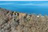 Aerial view showcasing the property's dramatic waterfront bluff setting, with open clearing near the shoreline, mature trees, and expansive open-water