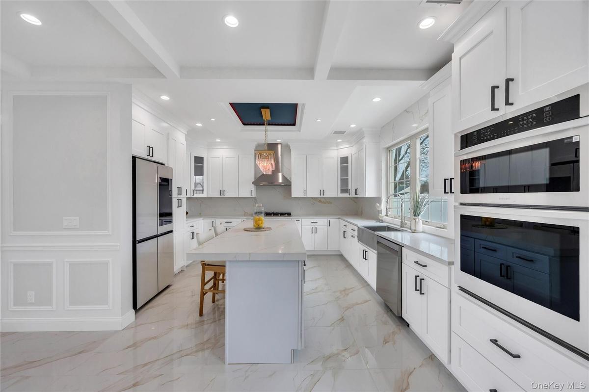 Kitchen with a breakfast bar, a sink, beamed ceiling, wall chimney exhaust hood, and appliances with stainless steel finishes