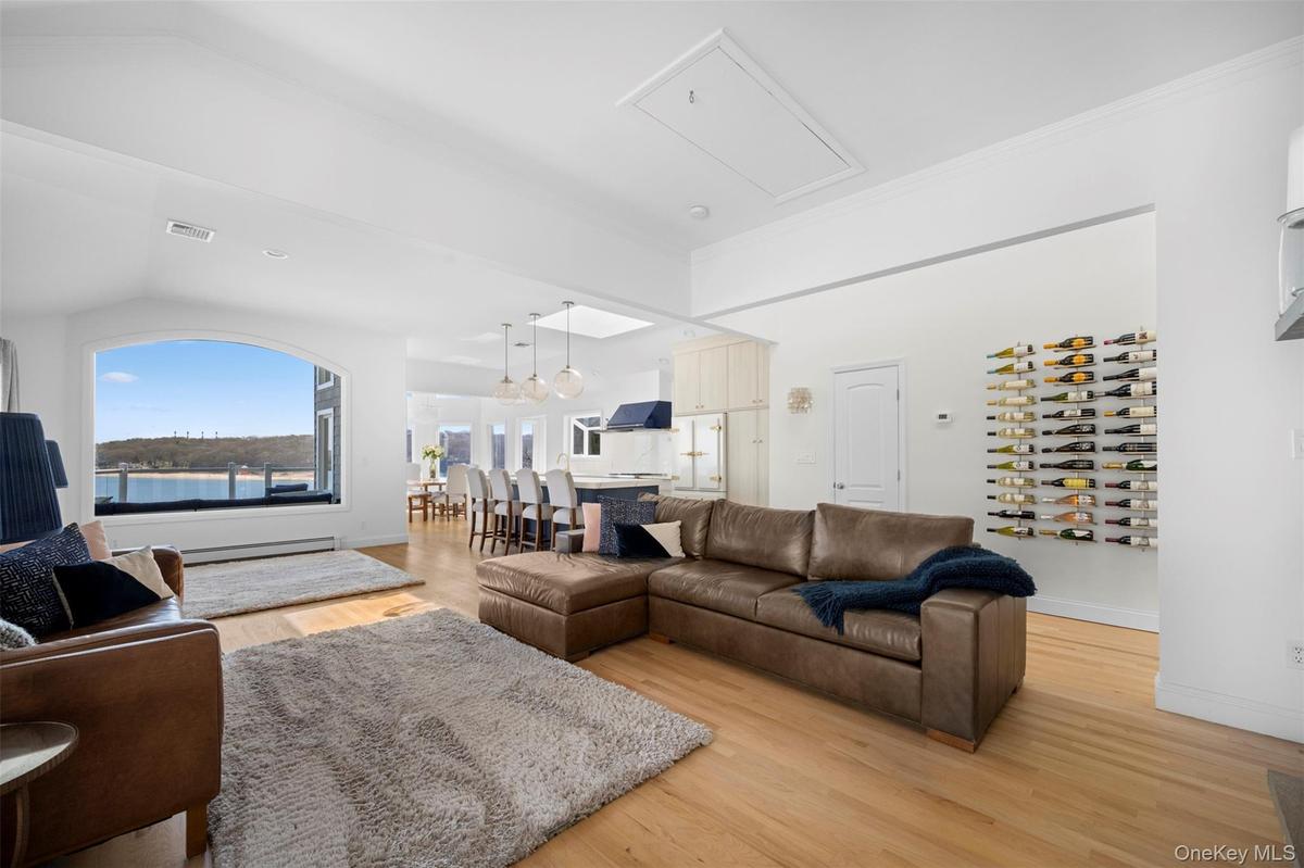 This spacious living area features hardwood floors, white walls, and a large arched window offering expansive water views