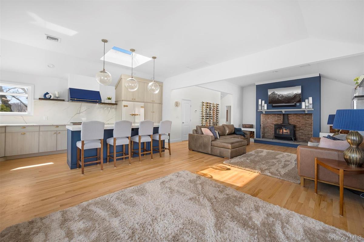 This open-concept living space features hardwood floors, a kitchen island with seating, pendant lighting, and a skylight