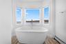 Bathroom with a white freestanding tub, large bay windows offering expansive water views.