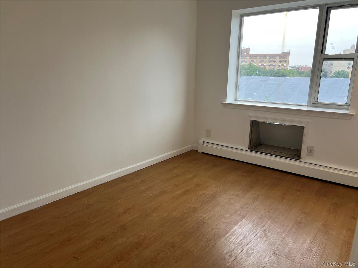 Empty room featuring healthy amount of natural light, wood finished floors, a baseboard heating unit, and baseboards