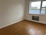Empty room featuring healthy amount of natural light, wood finished floors, a baseboard heating unit, and baseboards