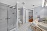 Bathroom with tile walls, tile patterned floors, wainscoting, vanity, and a stall shower