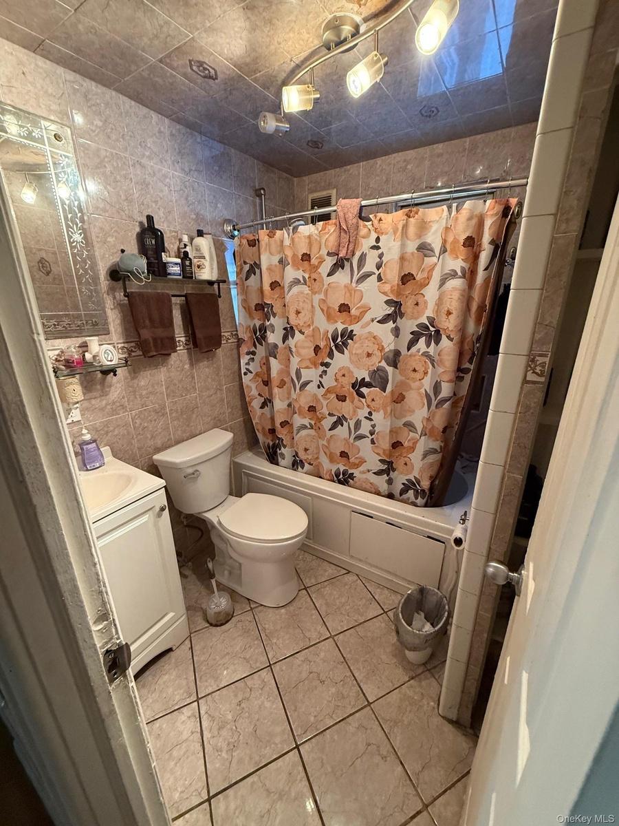 Bathroom featuring vanity, shower / bath combo with shower curtain, and tile walls