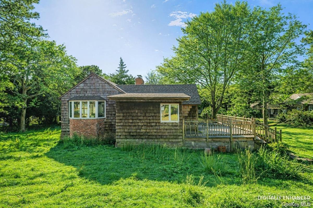 View of side of home with a yard, a wooden deck, and a chimney - Digitally Enhanced