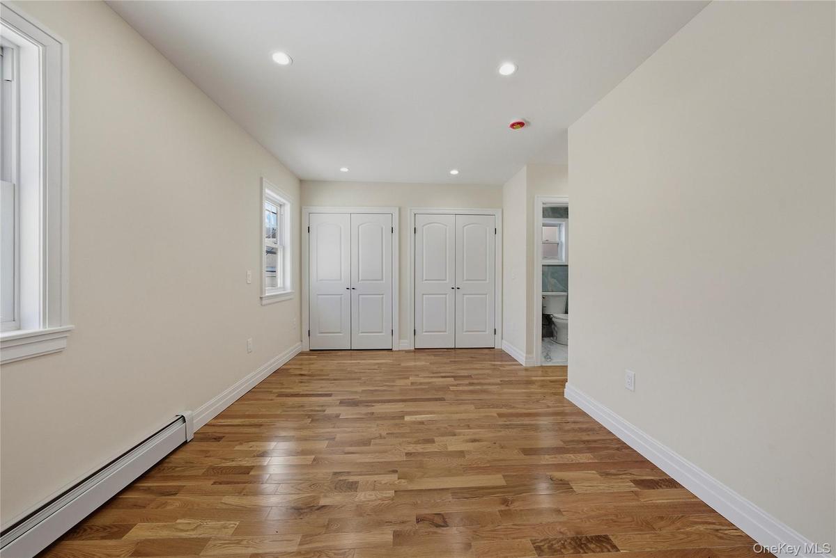 Unfurnished bedroom featuring baseboard heating, multiple closets, light wood-style flooring, recessed lighting, and ensuite bath