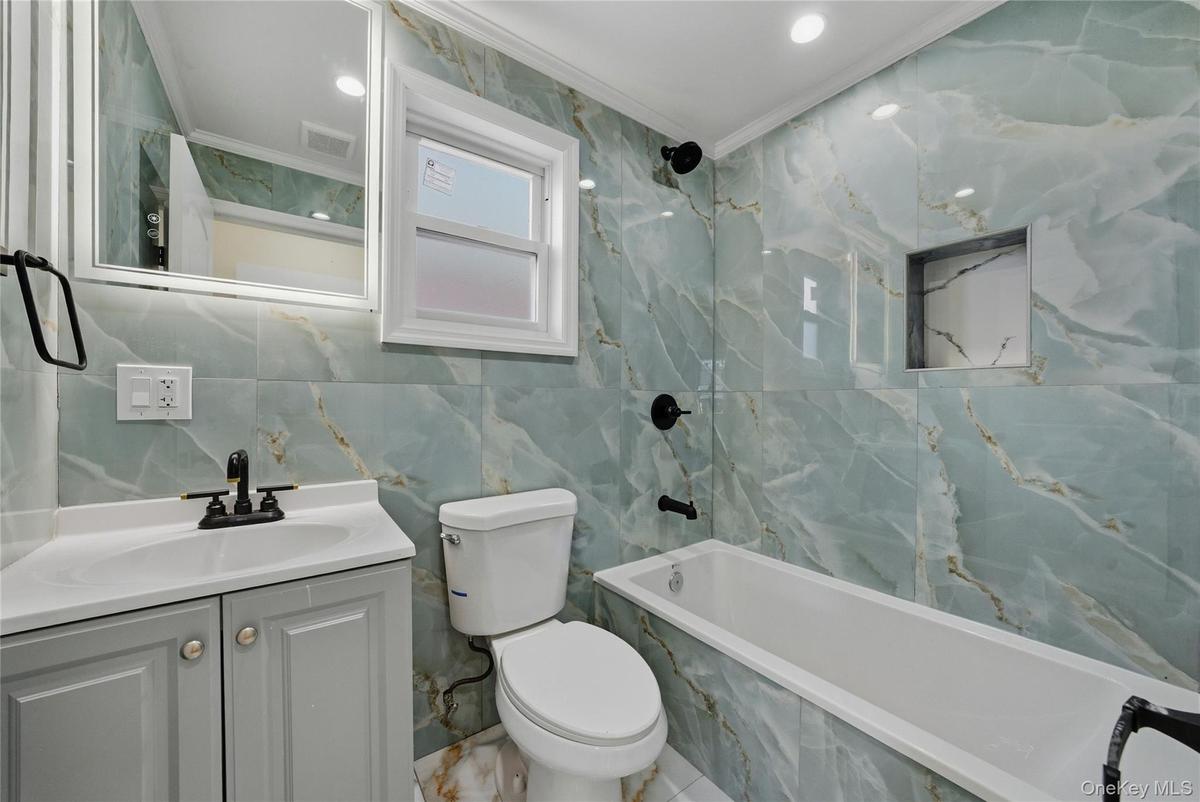Bathroom featuring ornamental molding, vanity, tile walls, a combined bath / shower with marble appearance, and recessed lighting