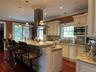 Kitchen with custom  cabinetry, light granite countertops, Turkish marble mosaic backsplash, crown molding, and island range hood