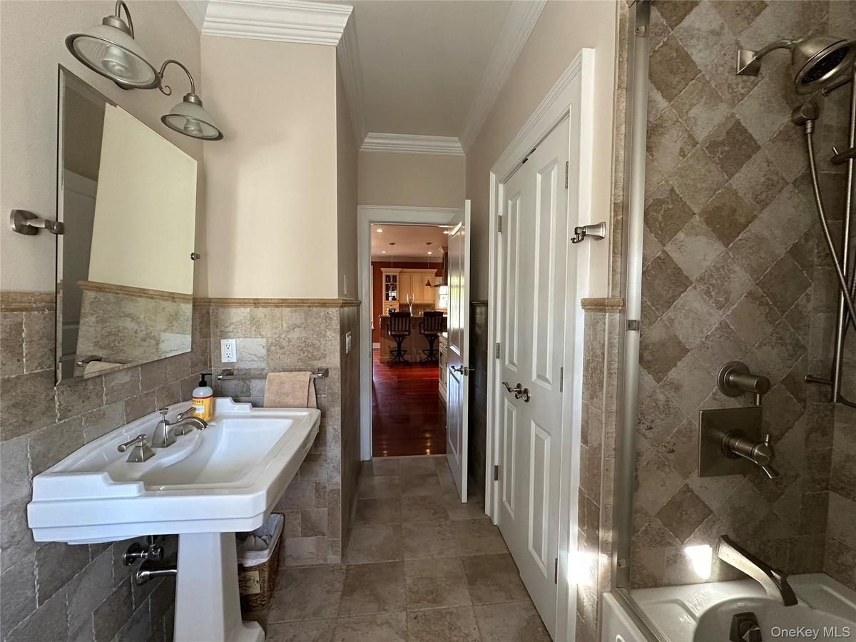 Full bath with tile walls, crown molding, a wainscoted wall, and bathing tub / shower combination