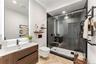 Modern ensuite bathroom in 2nd bedroom featuring a wood vanity with a white countertop, a rectangular mirror with backlighting, a glass-enclosed showe