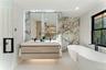 Full bathroom featuring double vanity, a freestanding bath, stone wall, and recessed lighting