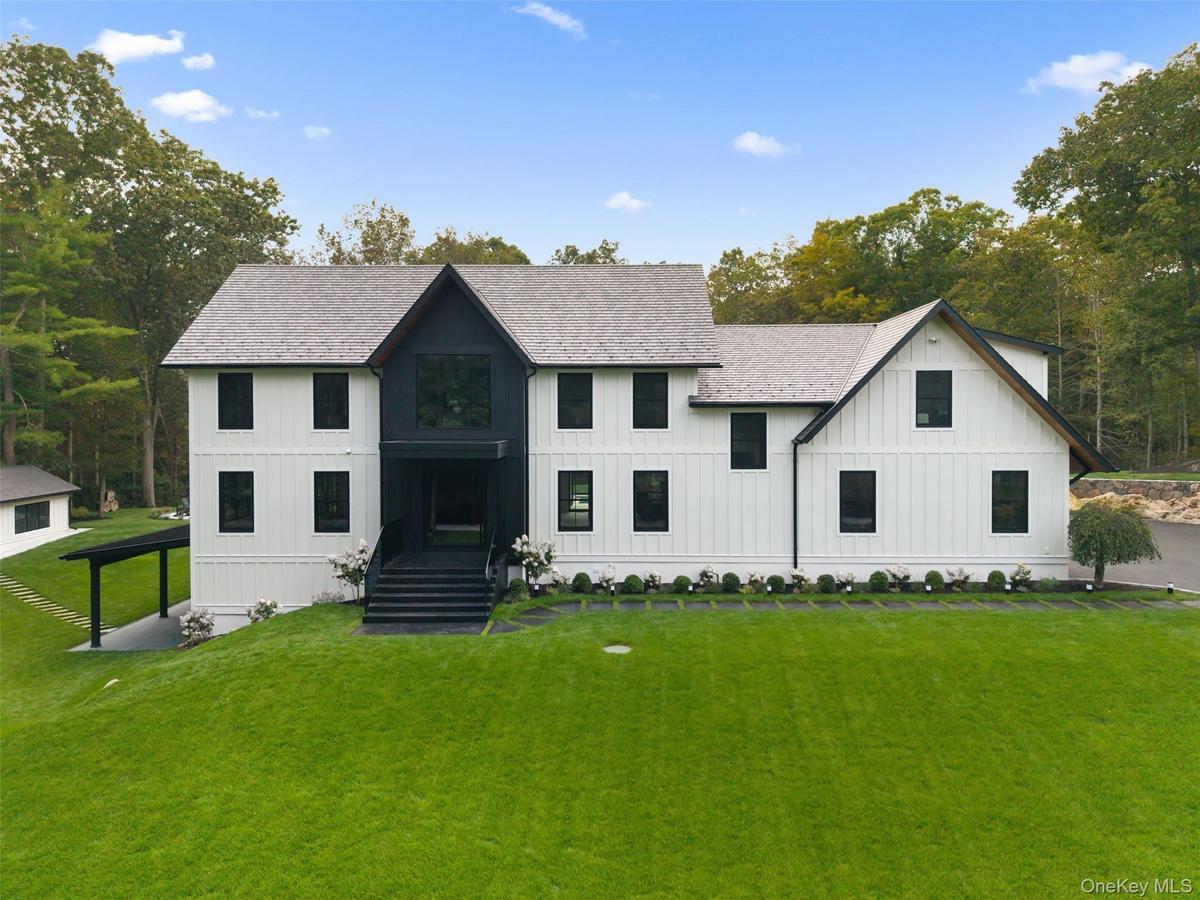 Modern inspired farmhouse with board and batten siding, a front yard, a shingled roof, and view of wooded area
