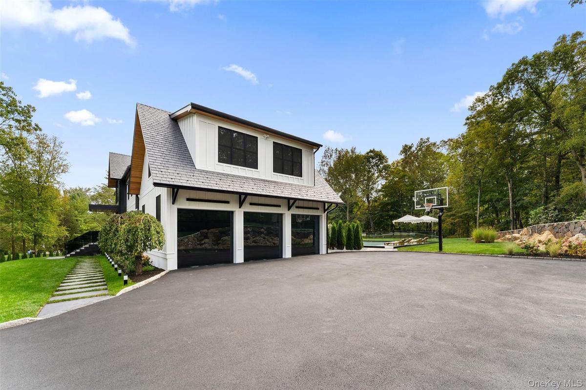 Three car garage attached to side of home with basketball hoop in long private driveway.