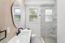 Bathroom featuring a sleek white vanity with a black faucet, a contemporary oval mirror, and a spacious shower with marble-look tiled walls and a clea
