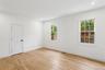 The room features light wood flooring, white walls, and two windows with white trim