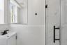 The bathroom features a modern vanity with a sink and a dark-toned faucet, a mirror, and a shower with a glass door and dark hardware
