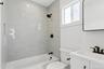 Bathroom featuring white subway tile in the shower, a window providing natural light, a white vanity with white countertop, and a black framed mirror