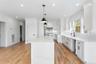 Modern kitchen featuring a large island, white cabinetry, integrated appliances, hardwood flooring, and a white tile backsplash