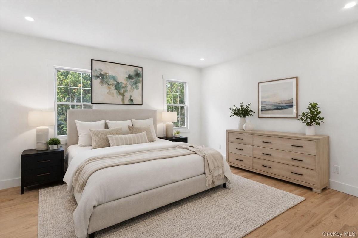 Staged Photo This bedroom features light wood flooring and white walls, creating a bright and airy atmosphere