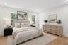 Staged Photo This bedroom features light wood flooring and white walls, creating a bright and airy atmosphere