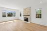 This bright living space features light wood flooring, a stone fireplace with a dark mantel, and multiple windows providing natural light