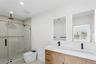 This bathroom features a spacious glass-enclosed shower with a rain showerhead, a dual vanity with rectangular sinks and dark fixtures, and illuminate