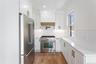 The kitchen features white cabinetry with gold-toned hardware, stainless steel appliances, light-colored countertops, and hardwood flooring