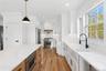 The kitchen features white cabinetry, hardwood floors, stainless steel appliances, and a kitchen island with a microwave