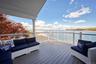 Spacious outdoor deck with an overhead roof, and a clear glass railing, offering expansive views of the water and distant shoreline