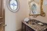 Powder room featuring an oval window, ornate framed mirror, granite countertop, undermount sink, and decorative vanity cabinetry