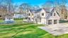 Contemporary shaker-shingle residence featuring a two-car garage with frosted glass doors, an expansive gravel driveway, and a fenced-in swimming pool