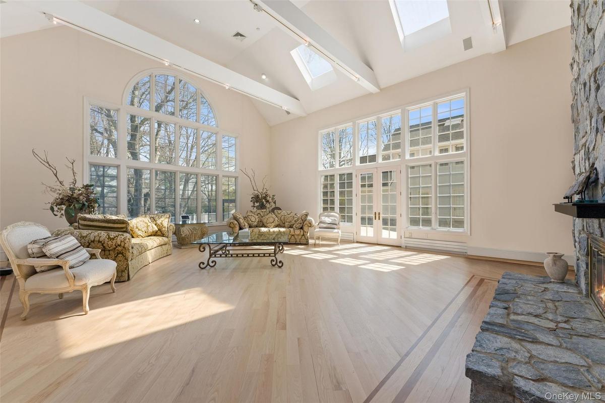 Living room with vaulted ceiling, light wood-type flooring, a stone fireplace, and a skylight