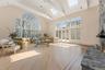 Living room with vaulted ceiling, light wood-type flooring, a stone fireplace, and a skylight