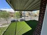 Covered outdoor balcony featuring artificial turf flooring, white metal railing, and a brick support column