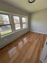 Room featuring three large windows, natural wood-finish flooring, light gray wall paint, white trim, and a ceiling-mounted light fixture